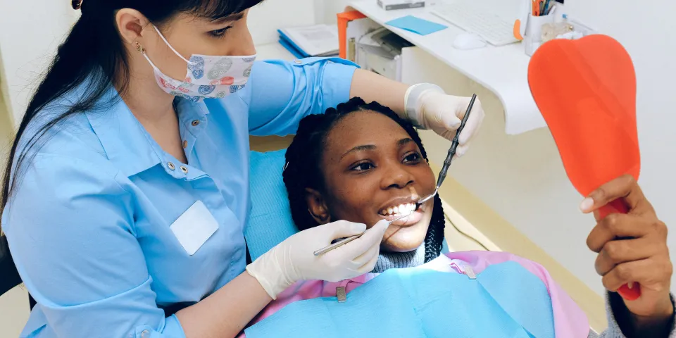 smiling dental patient in chair holding mirror